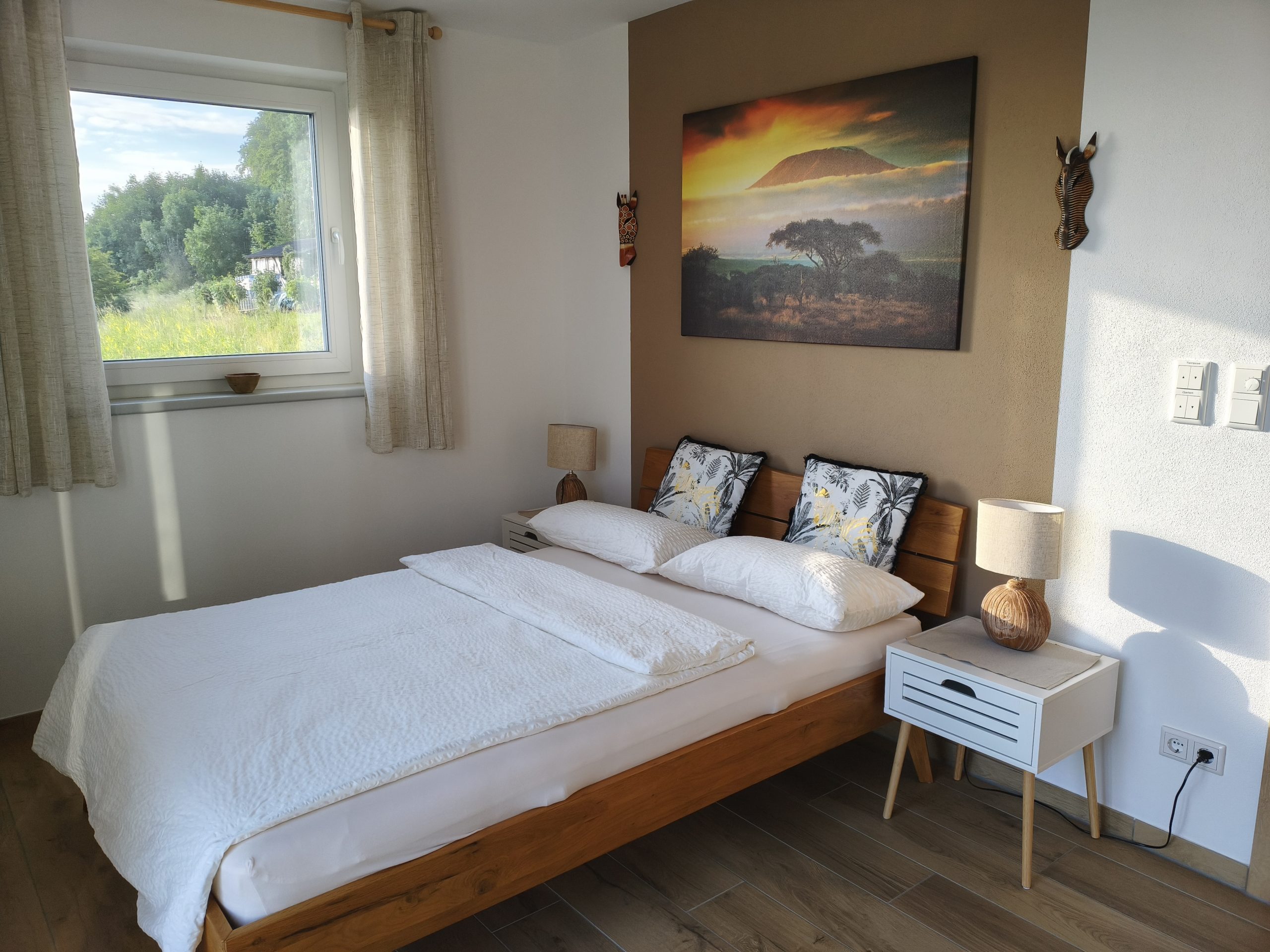 Helles Afrika-Schlafzimmer mit gemütlichem Doppelbett und Aussicht Afrika-Schlafzimmer mit Doppelbett, großem Wandbild und Blick ins Grüne