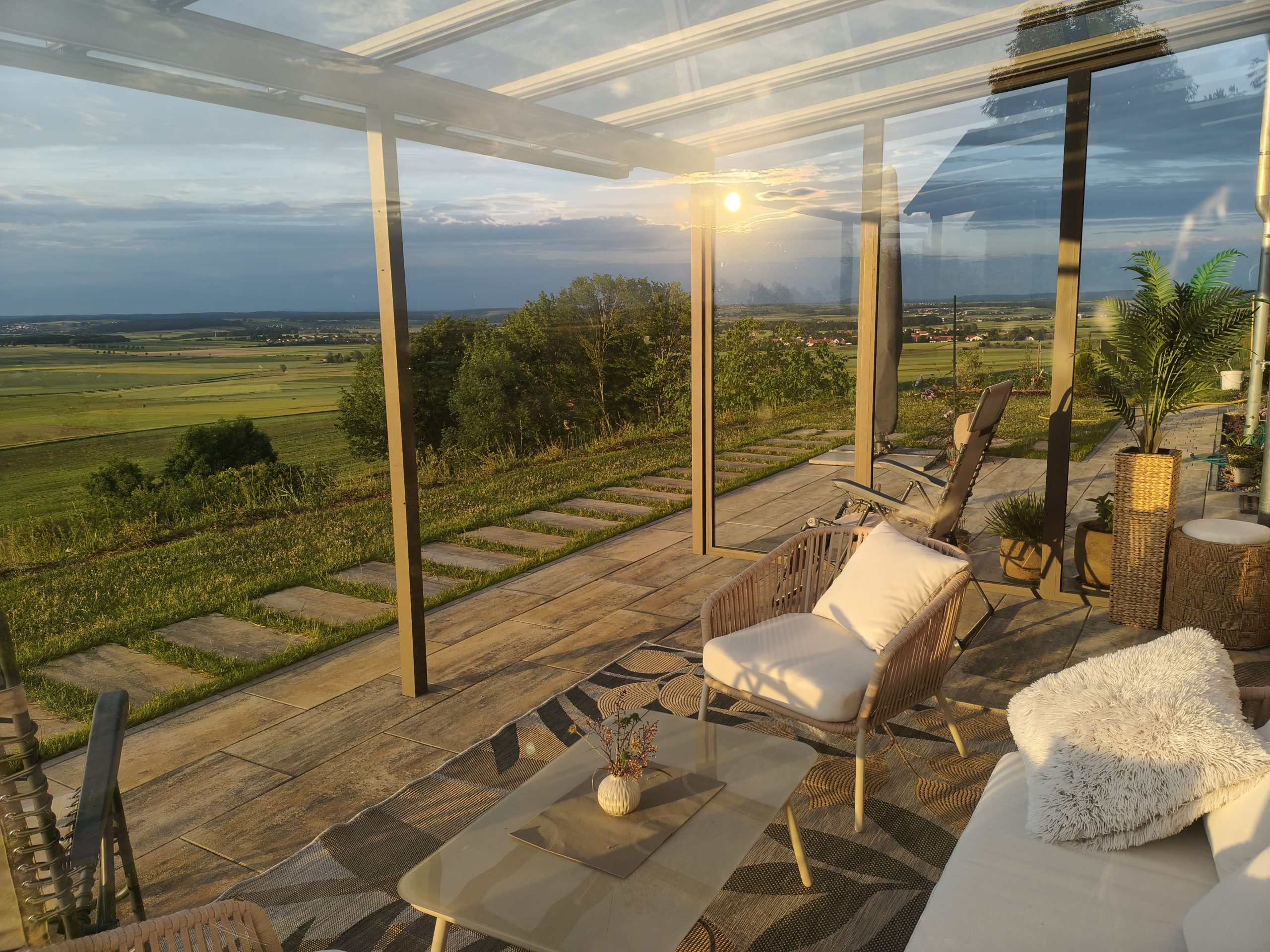 Panoramaterrasse mit Lounge und weitem Blick in die Landschaft Überdachte Panoramaterrasse mit Lounge und weitem Landschaftsblick bei tief stehender Sonne